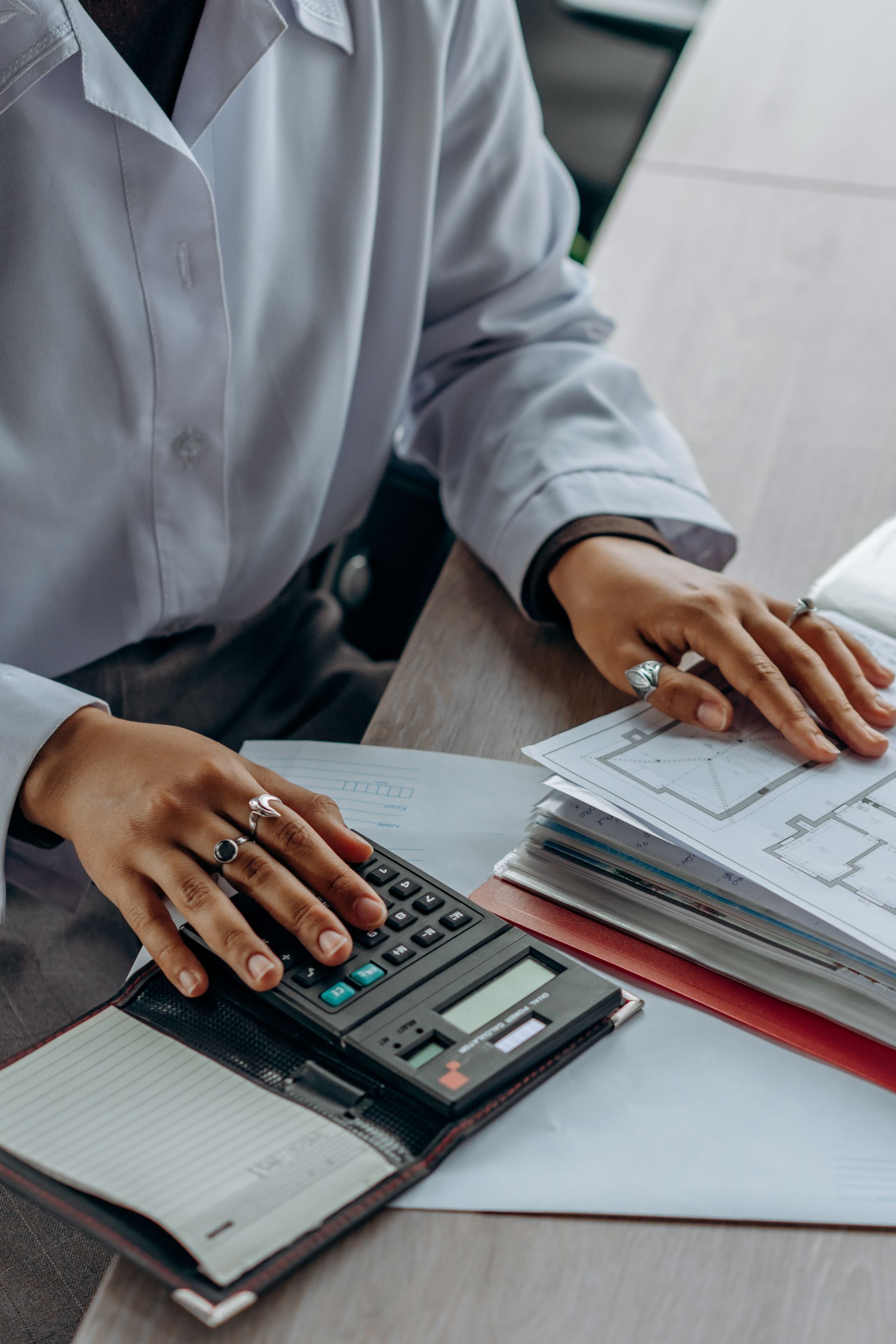 Une personne compare des plans de construction avec une calculatrice.